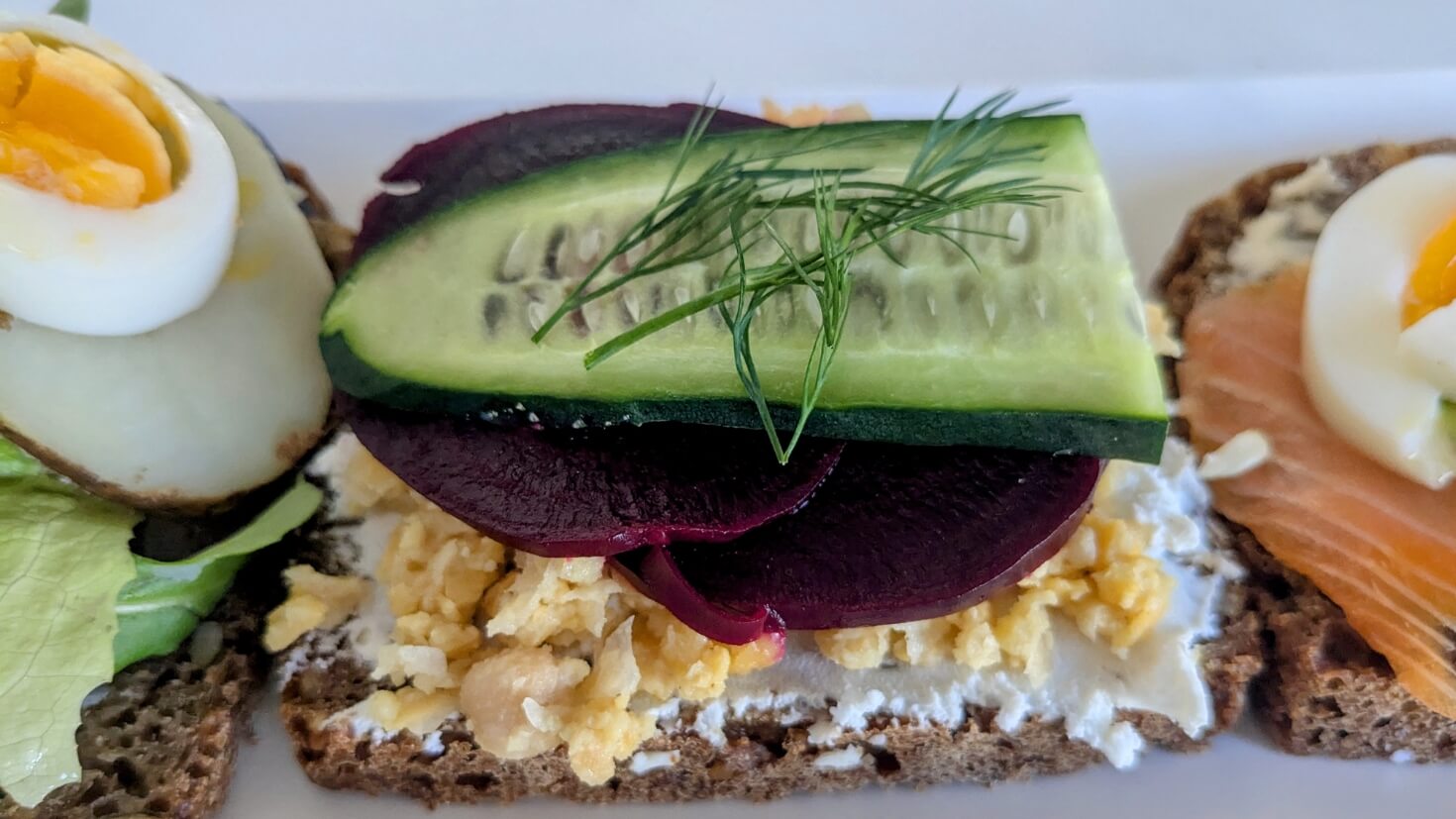 Danish smørrebrød with roasted beets, chickpeas, goat cheese, cucumber, and dill on dark rye bread (rugbrød)