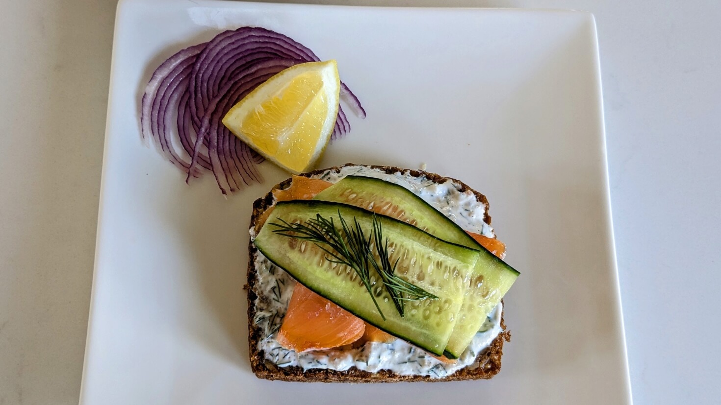 Danish smørrebrød with smoked salmon, cucumber, dill, and Nordic dill and horseradish sauce on dark rye bread (rugbrød)